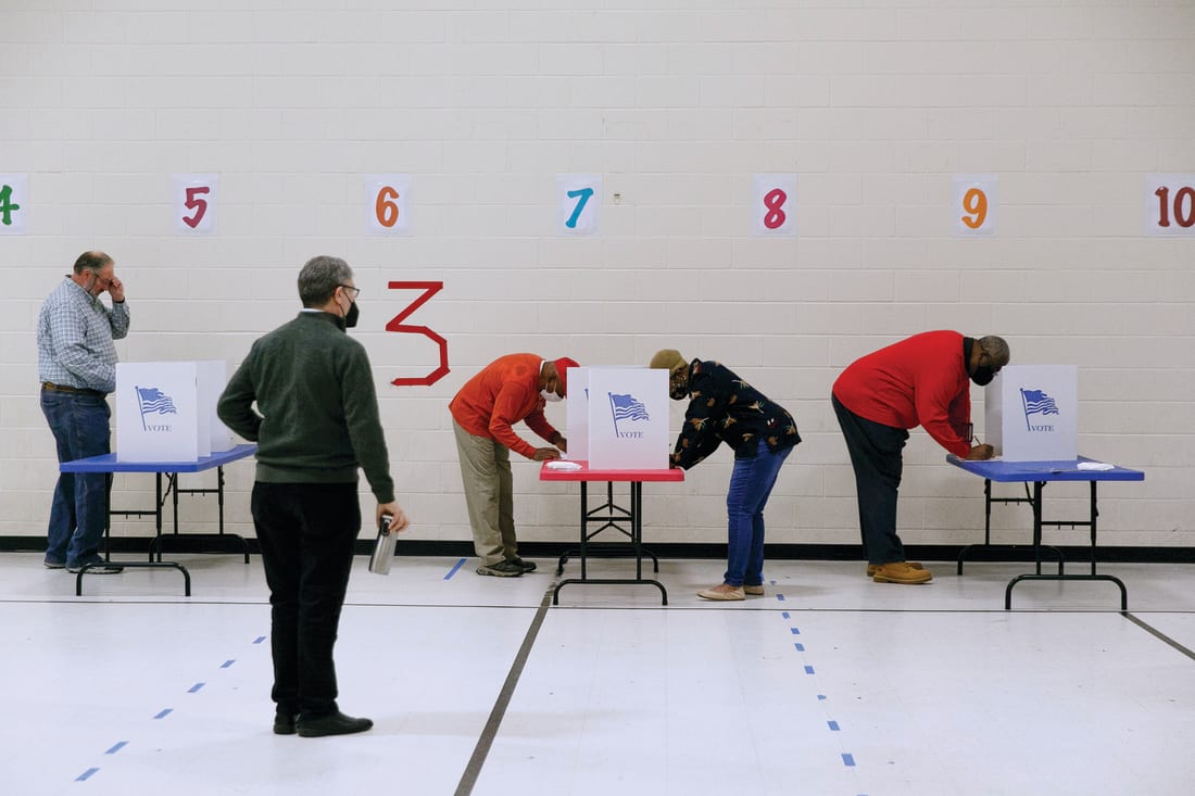 A poll watcher looks on as people vote in voting booths.