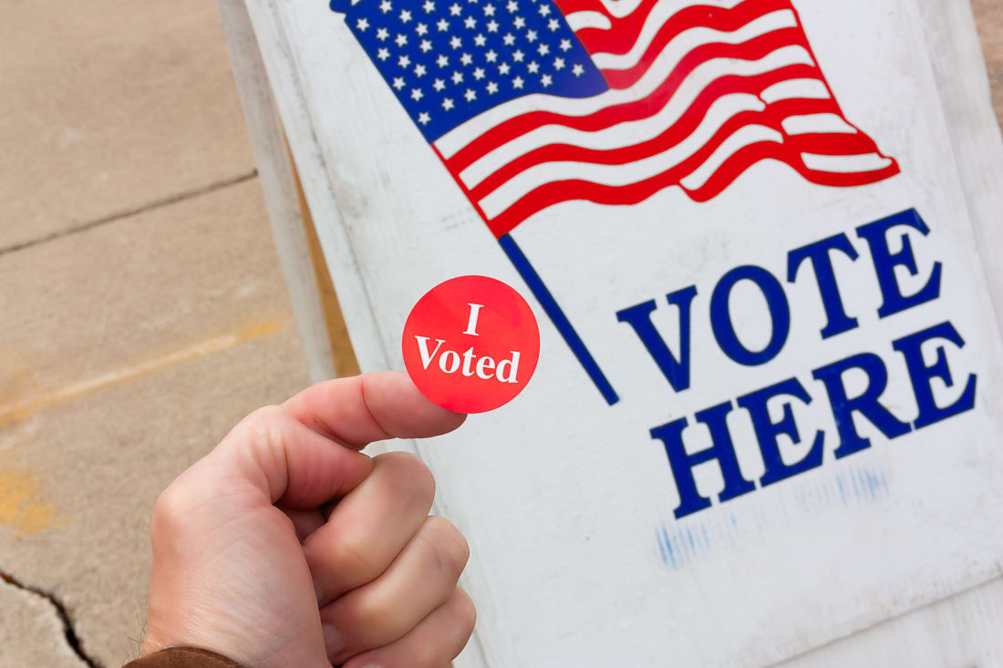 hand holding an "I Voted' sticker at outside of a polling place