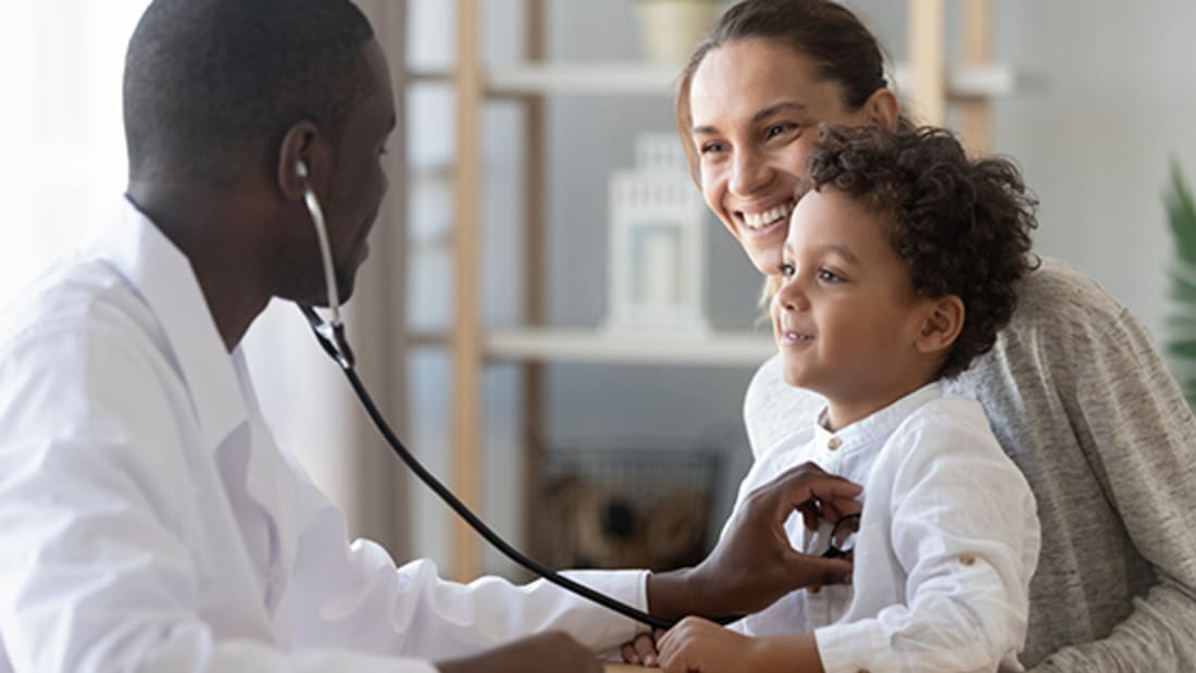 Male pediatrician holds stethoscope up to child's chest