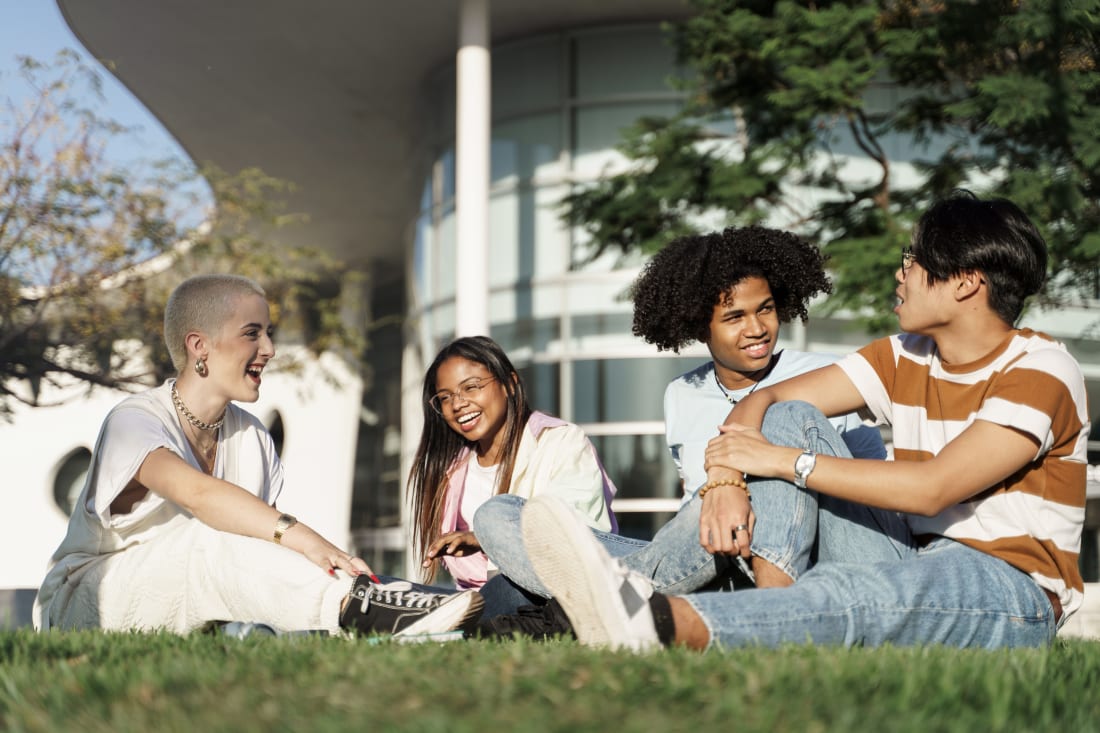 Group of multiracial teenager student friends sitting on the grass in the city park