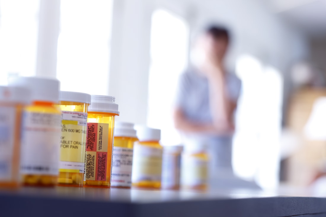 prescription pill bottles in foreground, blurry male figure in background
