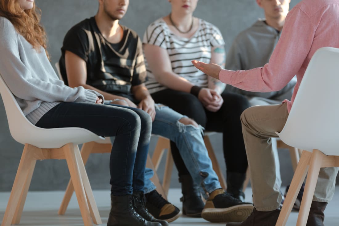 Group of young people sitting in a circle and talking during a therapy session