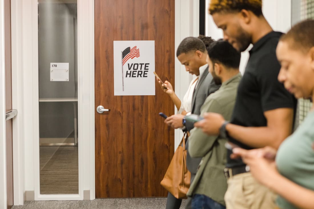 people looking at phones while waiting in line to vote