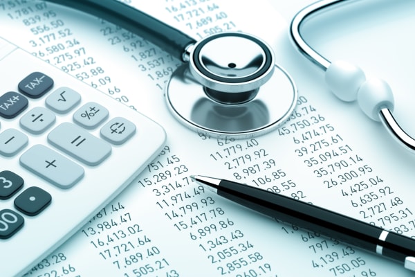 a cost balance sheet with a calculator and stethoscope on top