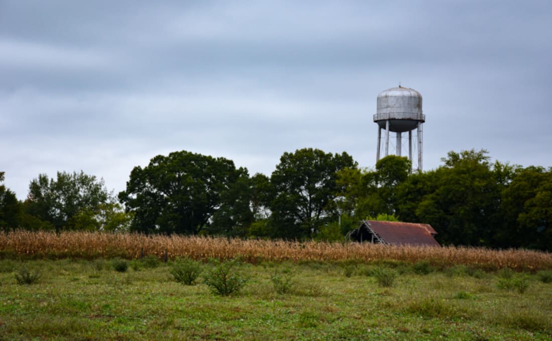 A water tower stands above a field with a barn roof seen below