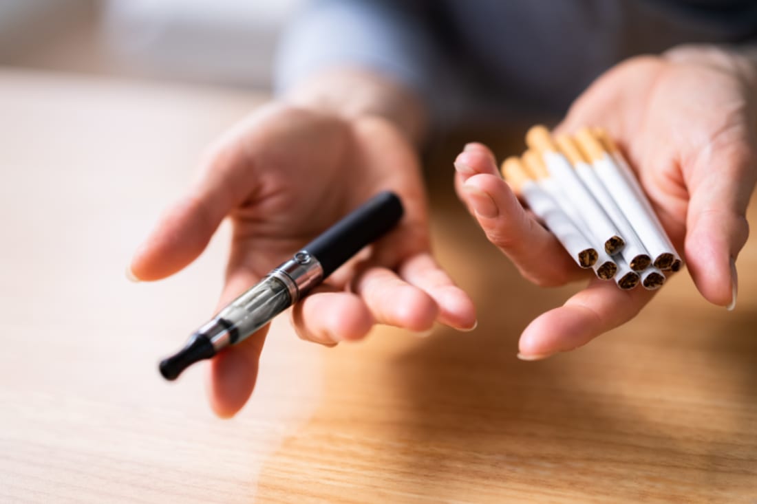 Woman's hand holding vape and tobacco cigarettes over wooden desk