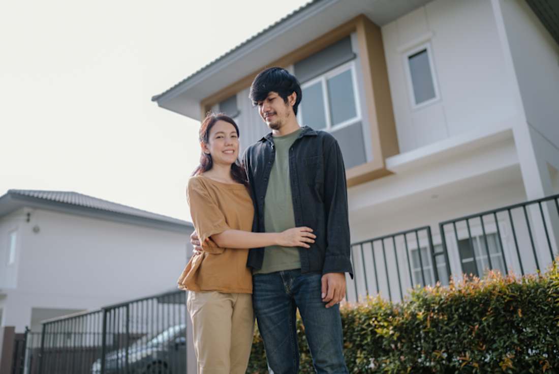 Happy young woman and man stand outside in front of their recently purchased home 