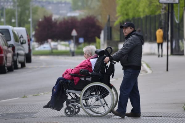 Elderly woman in wheelchair being helped across the street by caregiver