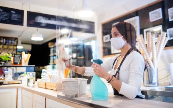 Young woman with face mask disinfecting counter inside cafe
