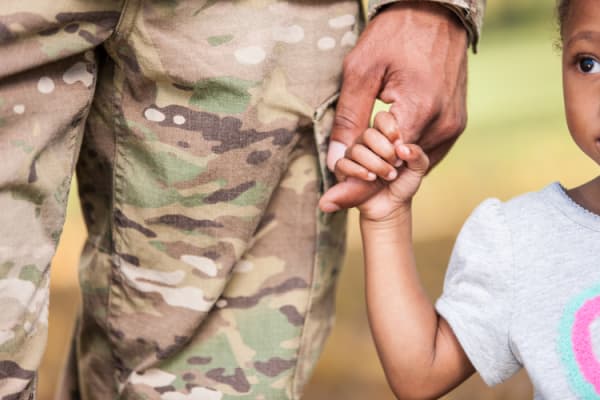 Closeup of a young black girl holding on to her military father's finger