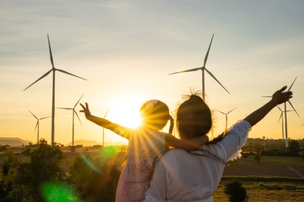 Mother and young daughter looking at wind generators turbines at sunset