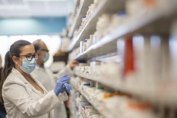 Hispanic pharmacist reaches for a prescription bottle off of a pharmacy shelf