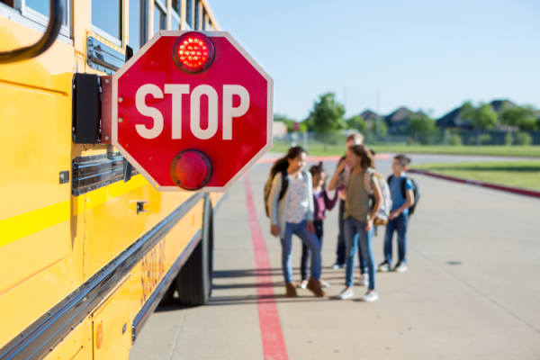 School bus stop sign out and lit with children crossing the road